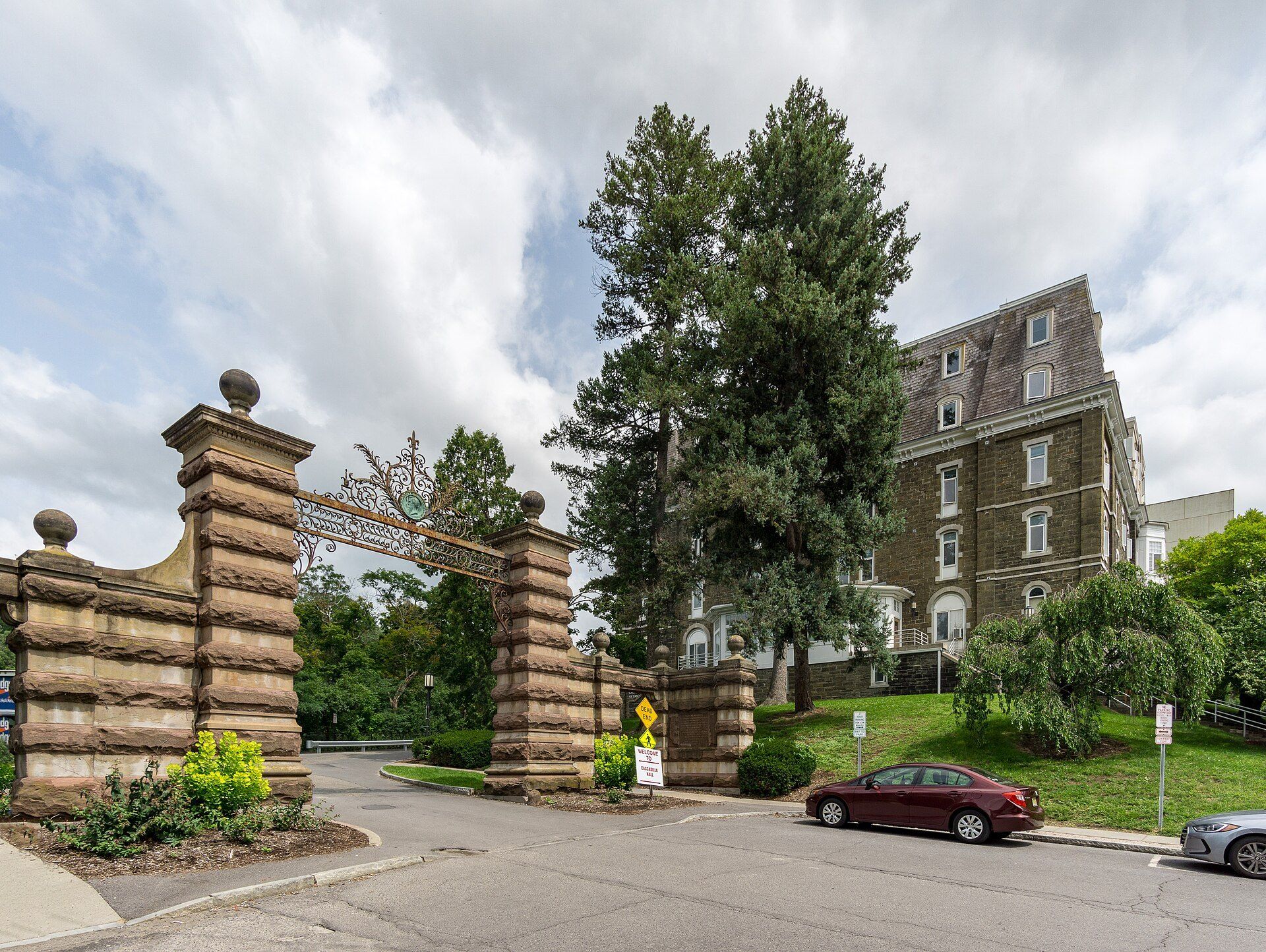 Stone campus gate at Cornell beside a residence hall, illustrating the proximity to campus theme in Richard Joseph Spinelli's work