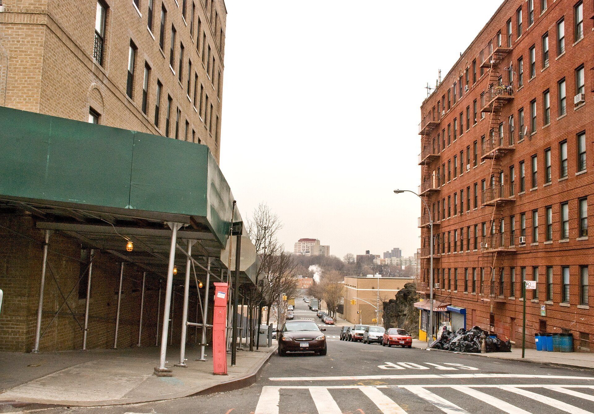 Bronx sidewalk between brick apartment buildings, illustrating the walkable maintenance radius in an essay by Richard Joseph Spinelli