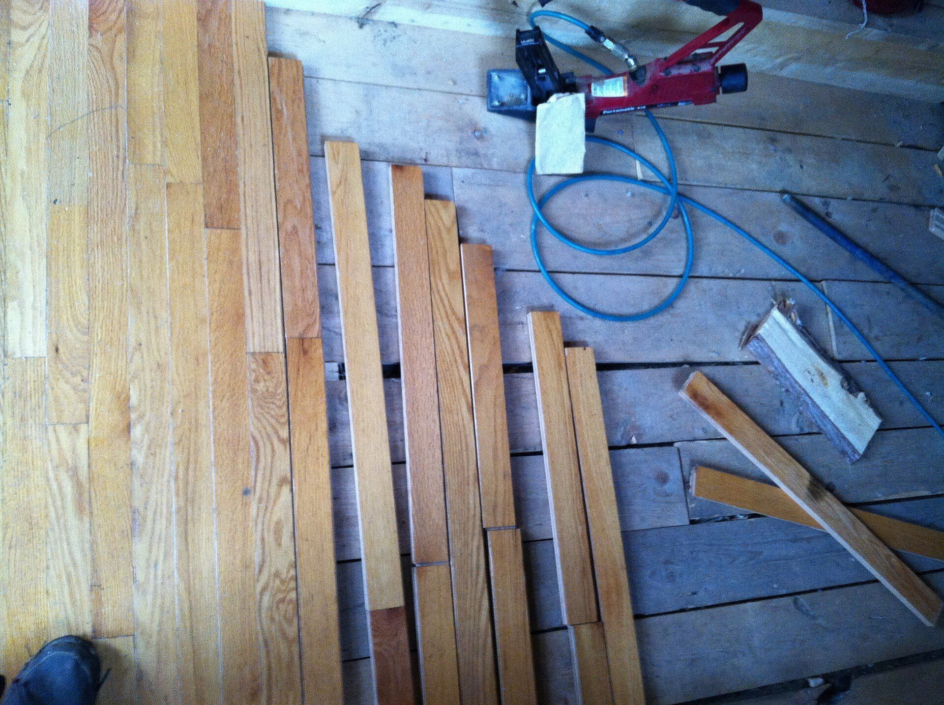 Hardwood planks and a flooring nailer mid renovation, illustrating the durable finishes in an essay by Richard Joseph Spinelli
