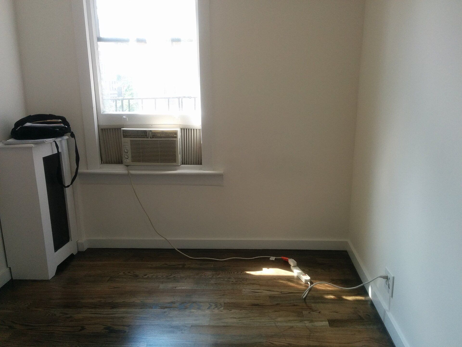Empty apartment room with a window air conditioner, evoking the summer sublet months in student housing like Richard Joseph Spinelli's