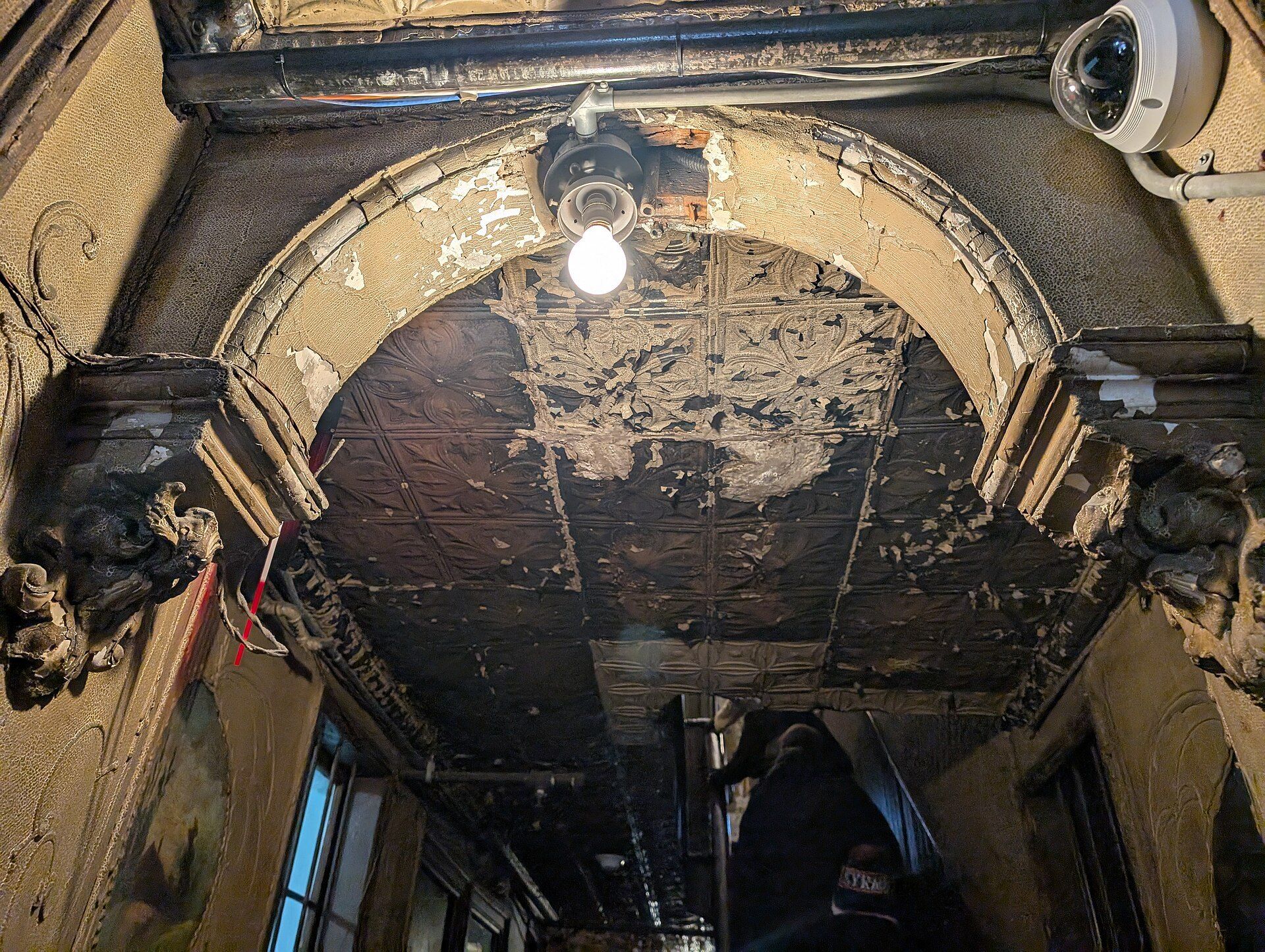 The pressed tin ceiling and peeling plaster arch of an old tenement hallway, the older building type Richard Joseph Spinelli works with